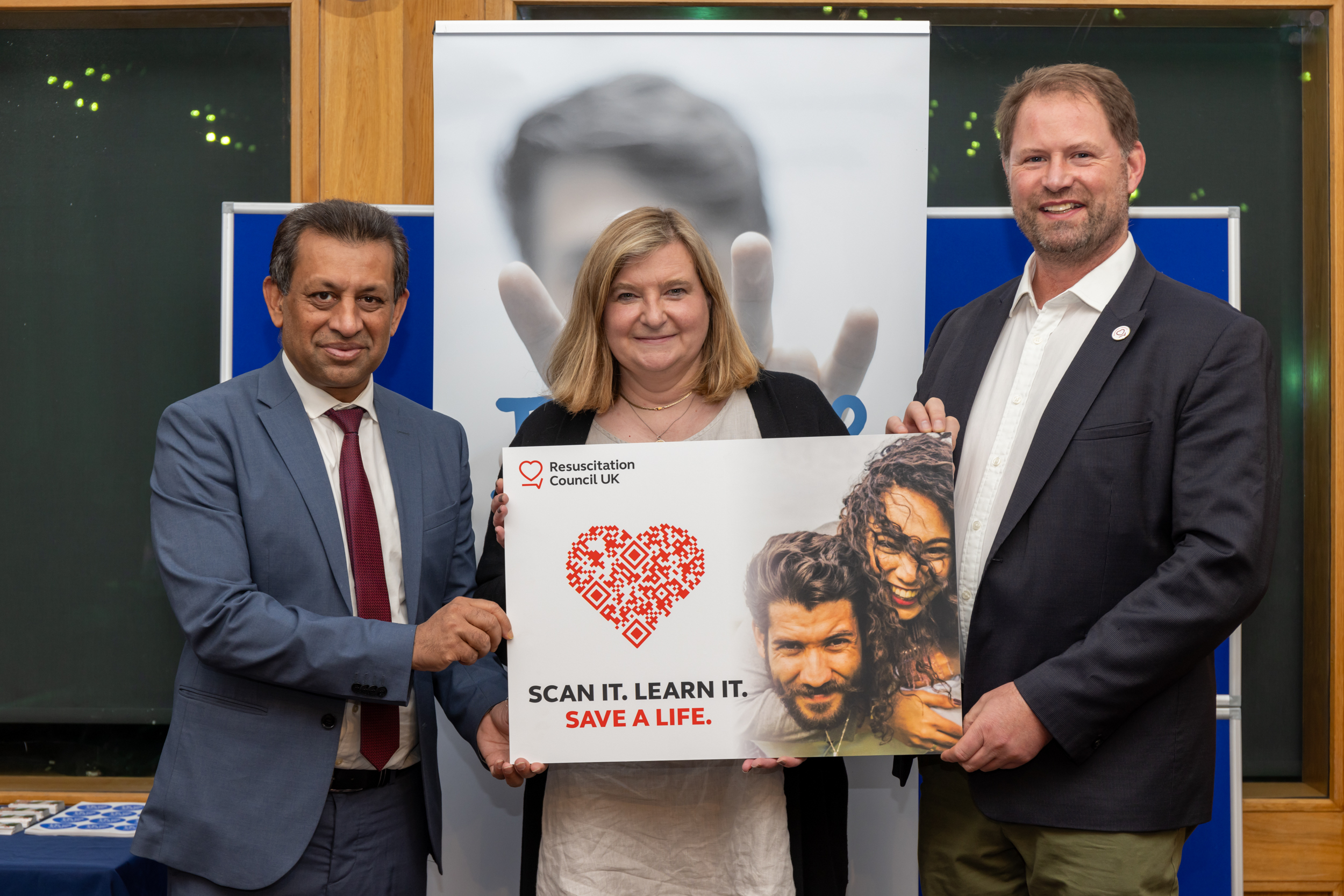 Two men and a woman smiling and holding a placard with a QR code and the text "Scan it. Learn it. Save a life."