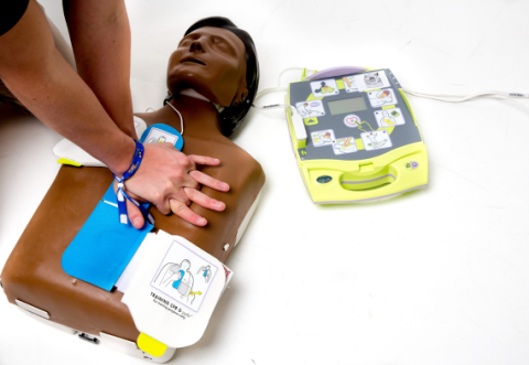 Person with hands interlocked, doing CPR on a mannequin with defib placed in position