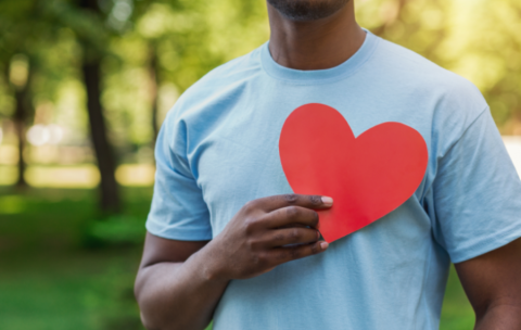 Image of man holding a red paper heart to their chest. 