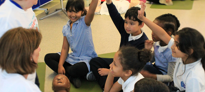 Children gather around a CPR manikin to learn CPR