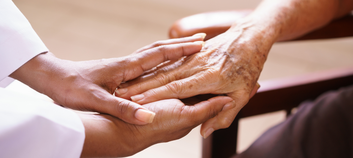 A carer places their hand on an older person's hand.