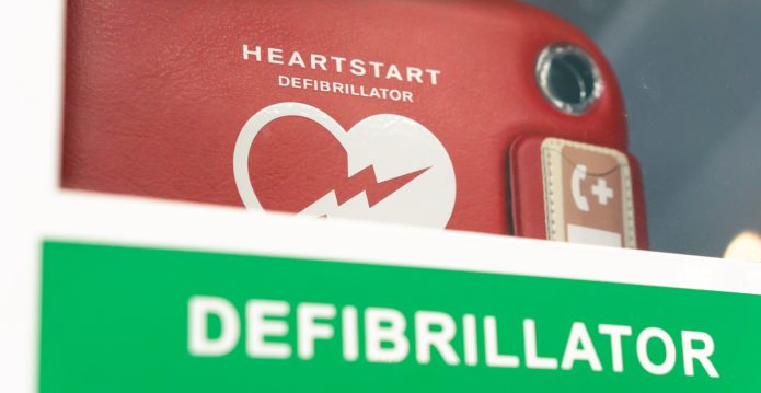 Image of a Red Defibrillator behind glass with a green label saying 'Defibrillator' on it