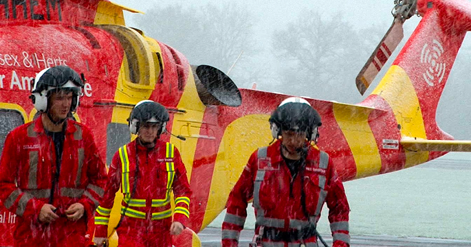 Three men standing outside in the rain, with a helicopter in the background